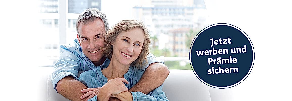 Content man hugging his wife on the couch smiling at camera at home in the living room